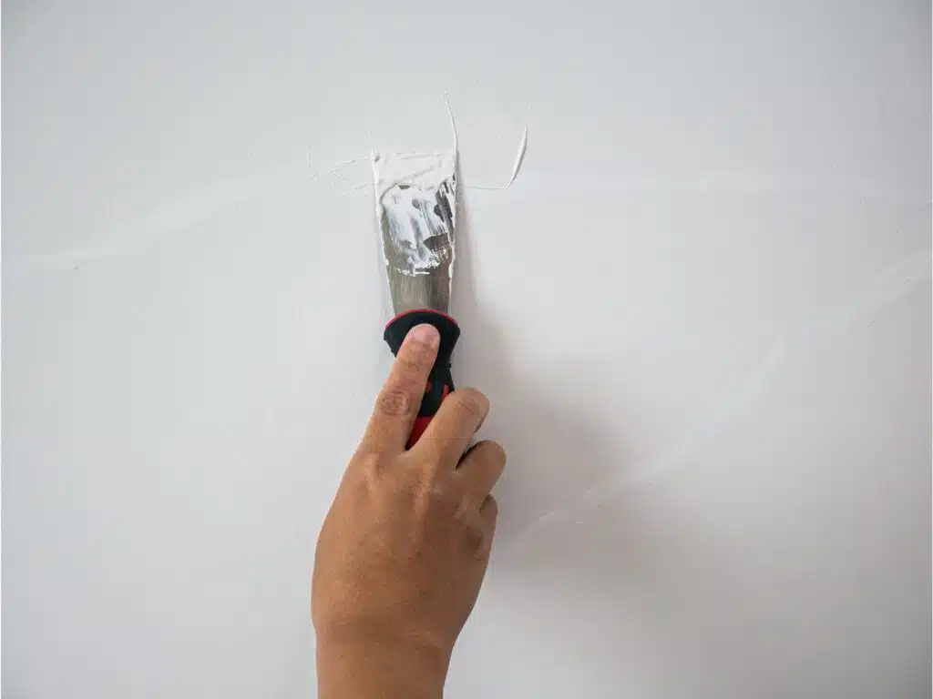 persona reparando grieta en pared con espatula